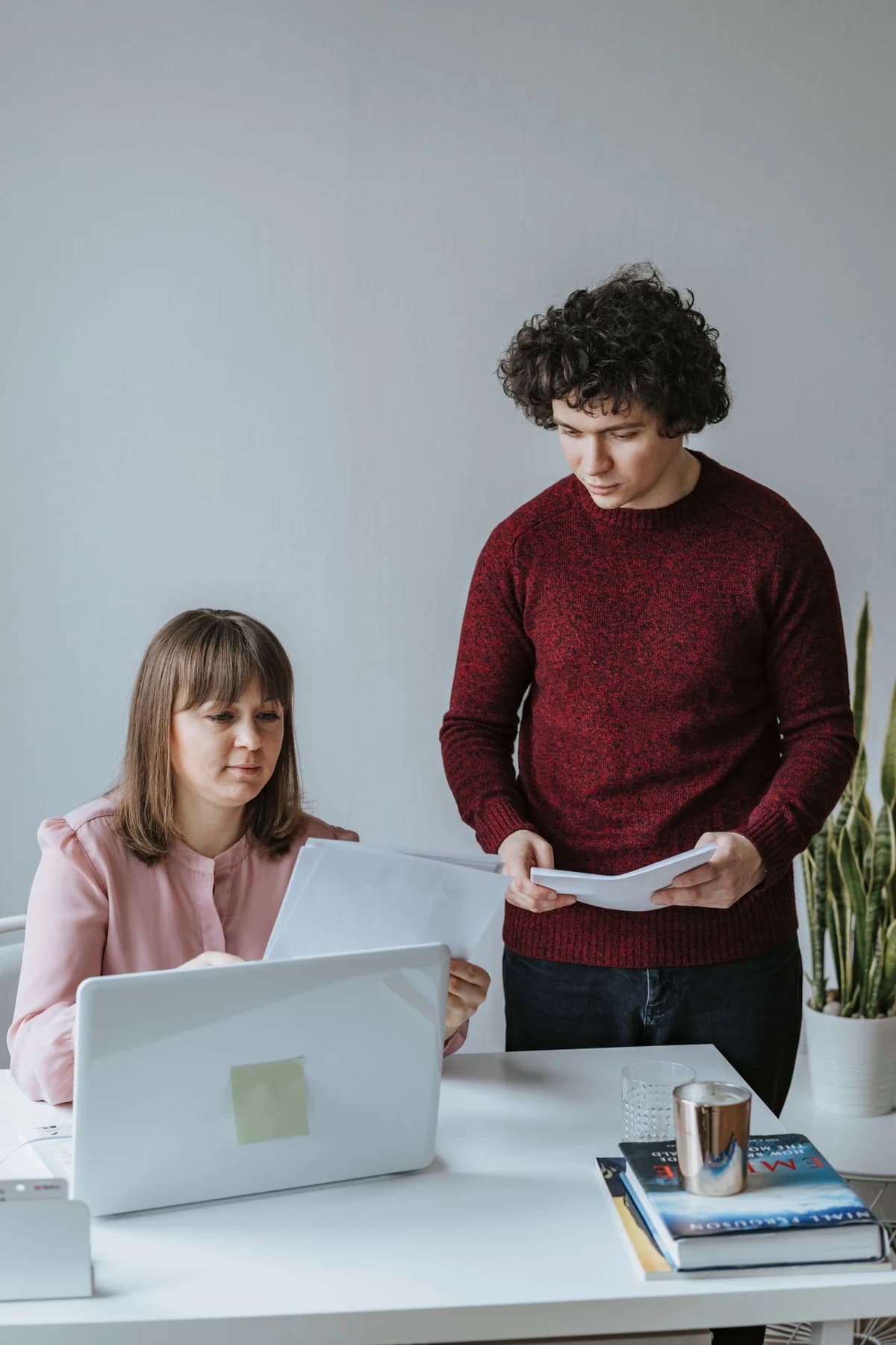 Two colleagues reviewing documents beside a laptop
